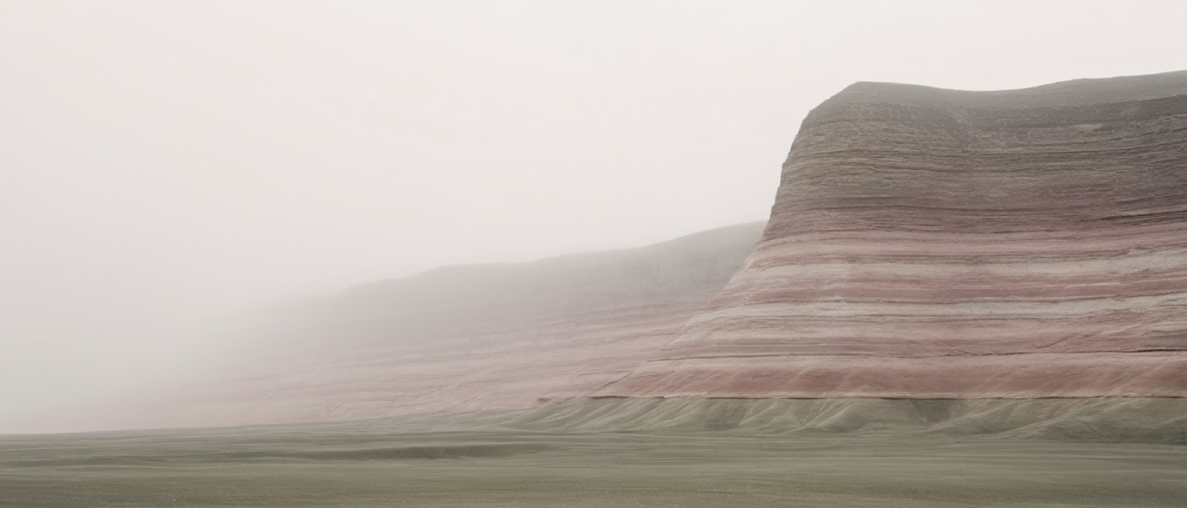 Layered sedimentary rock strata rising through morning haze